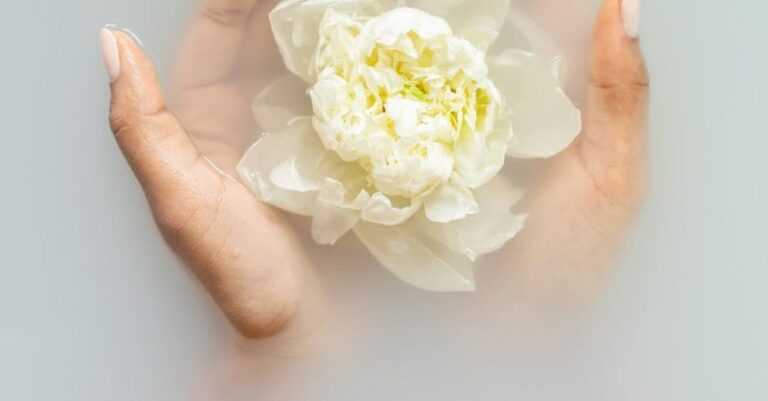 Moisturizers - Unrecognizable female with soft manicured hands holding white flower with delicate petals in hands during spa procedures