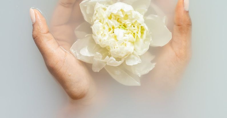 Moisturizers - Unrecognizable female with soft manicured hands holding white flower with delicate petals in hands during spa procedures