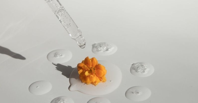 Serums - From above of drops of transparent moisturizing cosmetic product dripped by pipette and small fresh flower head placed on white table