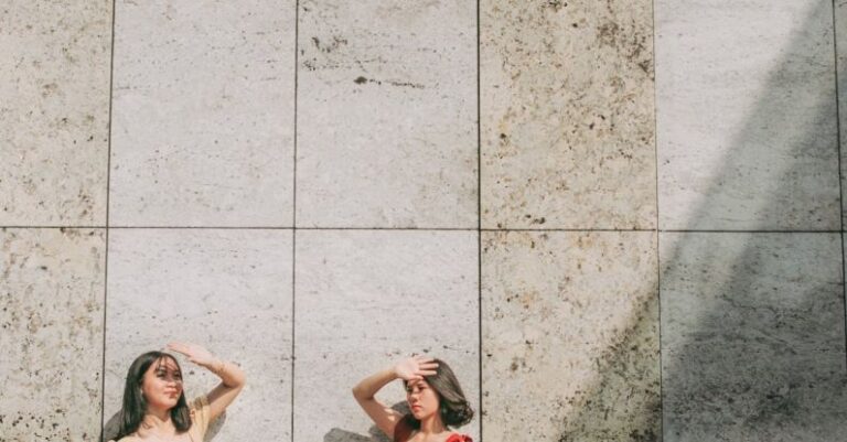 Sun Protection - Photo of Two Women Standing by Wall Posing While Blocking Sun with Their Hands